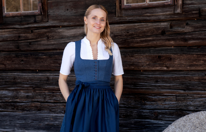 Frau in einem blauen Dirndl vor einer traditionellen Holzwand