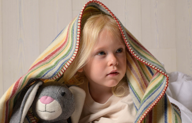 Kind unter einer gestreiften Wolldecke mit Kuscheltier