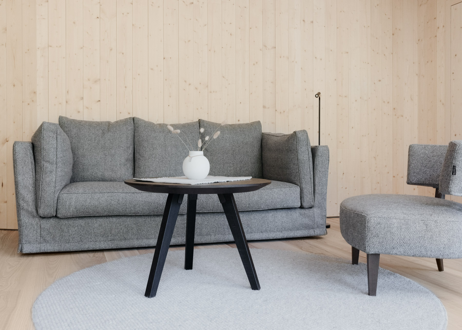 Wohnzimmer mit grauem Sofa, Sessel und rundem Tisch