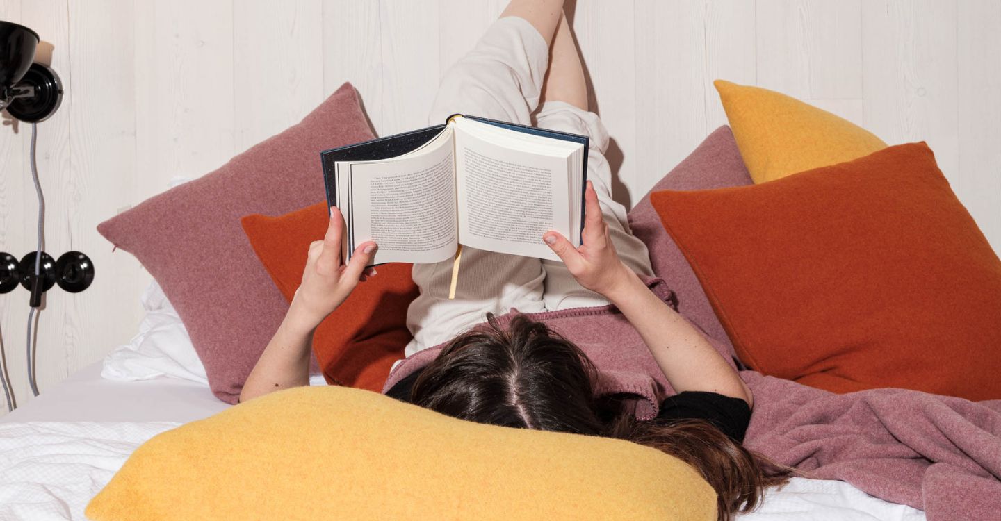 Person beim Lesen zwischen farbigen Wollkissen