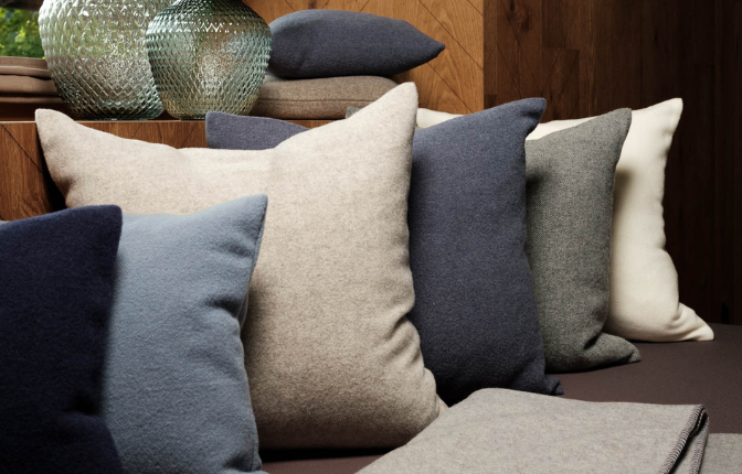 Verschiedene Wollkissen in Grau, Blau und Natur auf einem Sofa