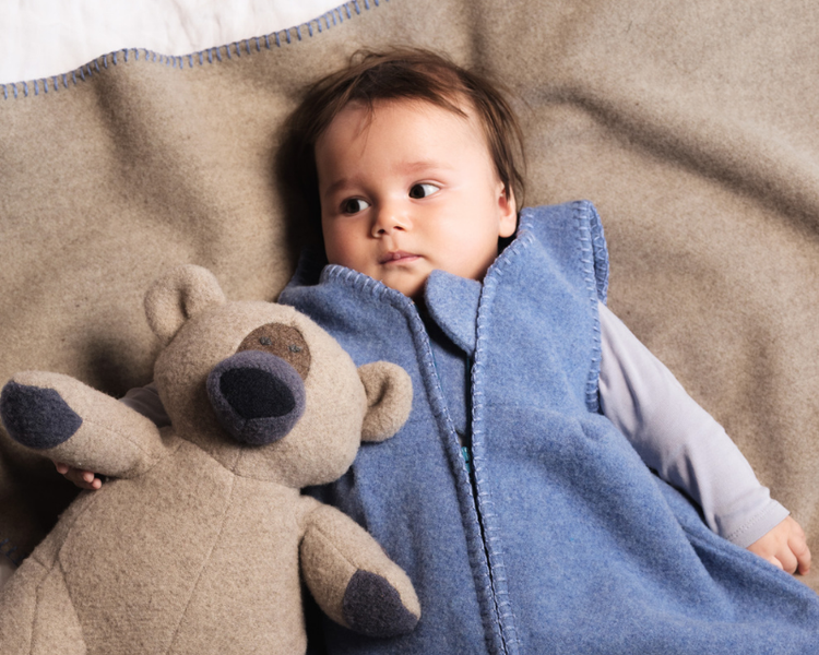 Baby im Wollschlafsack aus natürlicher Wolle neben Stoffbär – hochwertige Wollprodukte für Babys und Kinder von Steiner1888